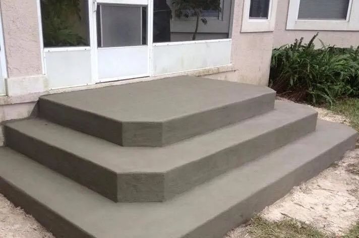A newly poured gray concrete two-step staircase leading to a house doorway with a screen door.