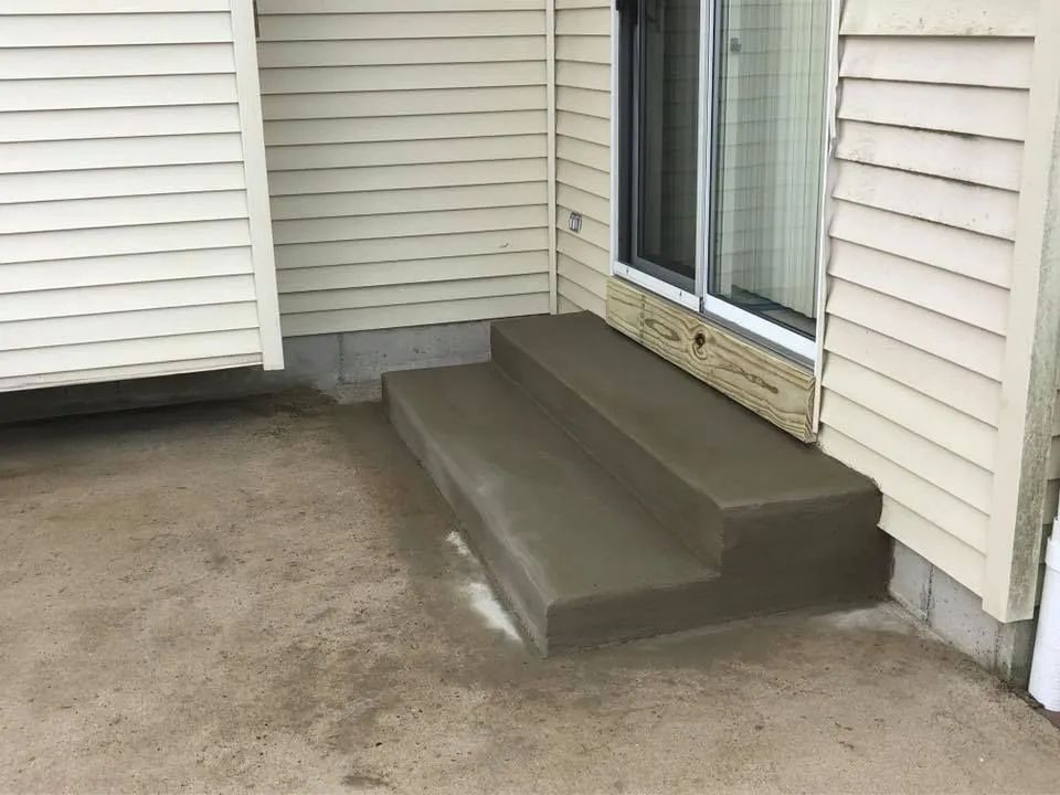 New concrete steps installed leading to a sliding glass door on the side of a house with beige siding.