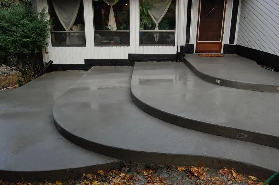 A set of curved, multi-level concrete steps leading to the front door and windows of a house.