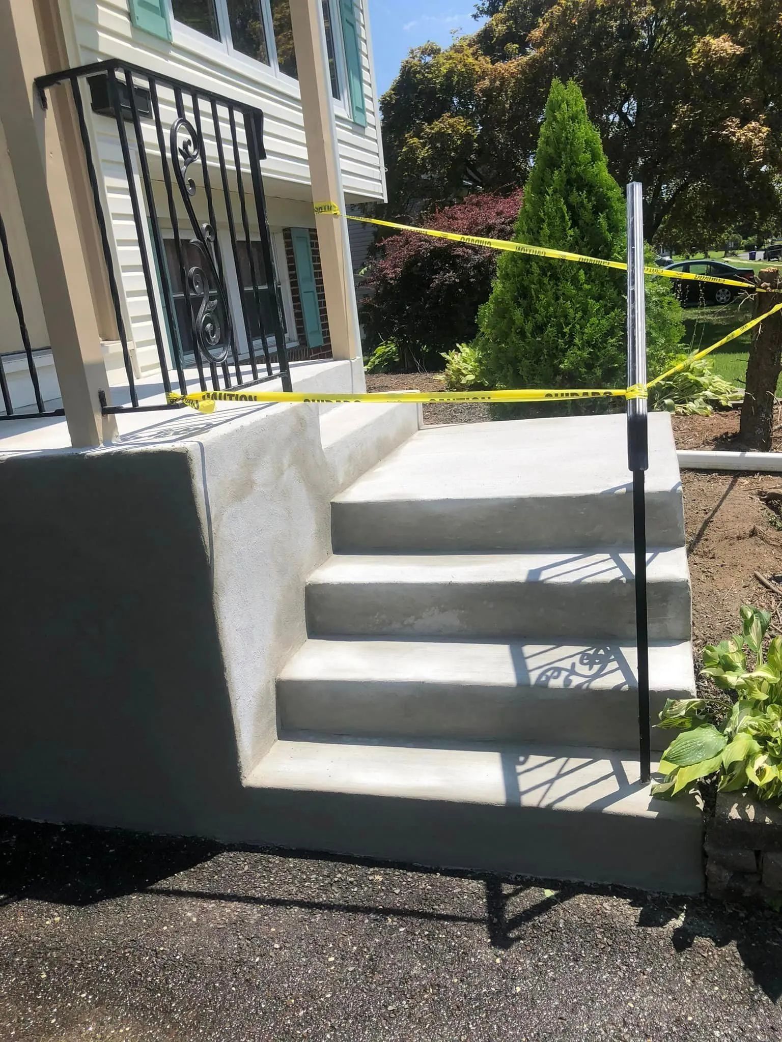 A newly poured concrete staircase with four steps leading to a porch, cordoned off with yellow safety tape.