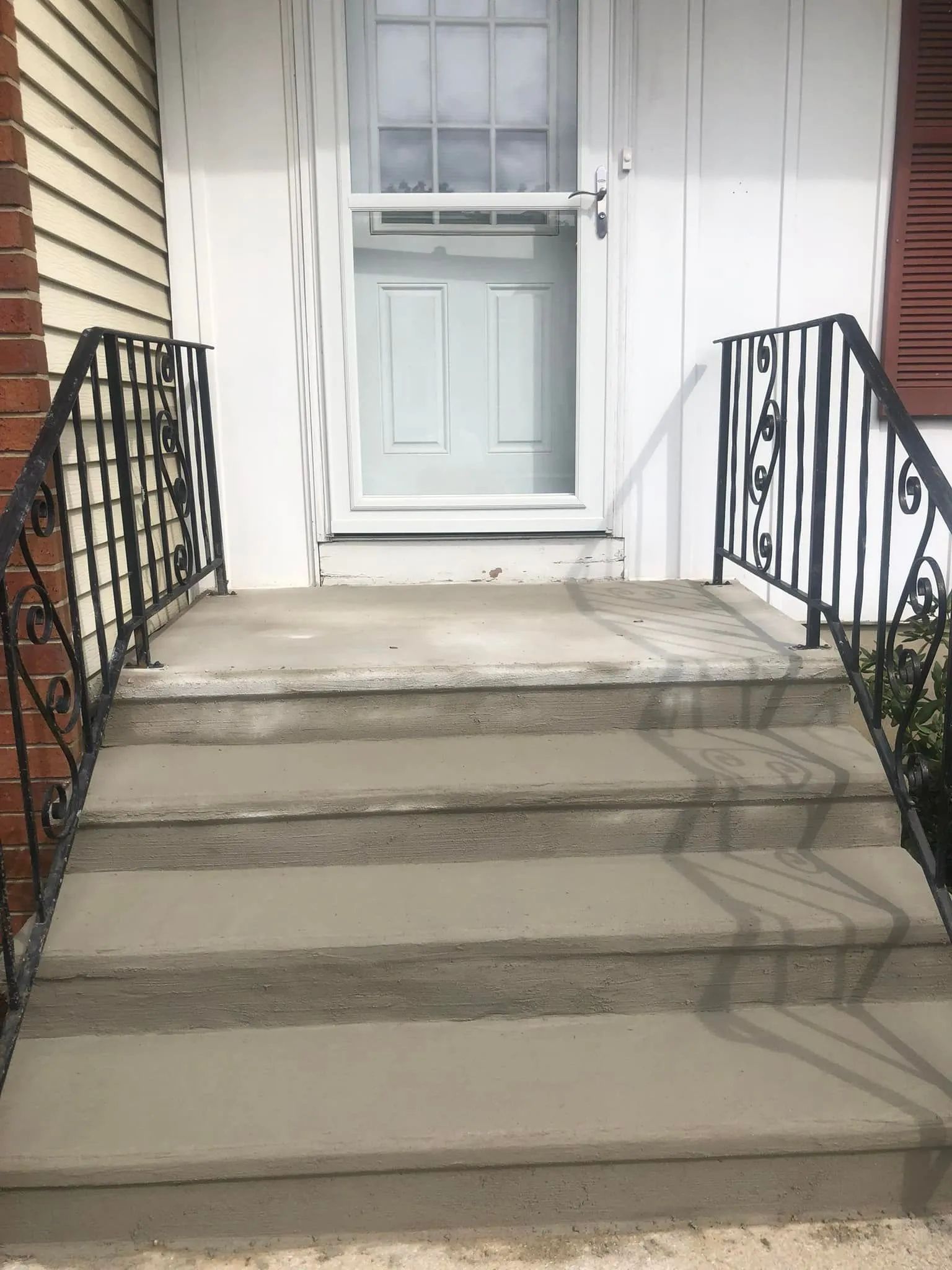A set of four concrete steps leading to a front door with black decorative metal handrails on both sides.