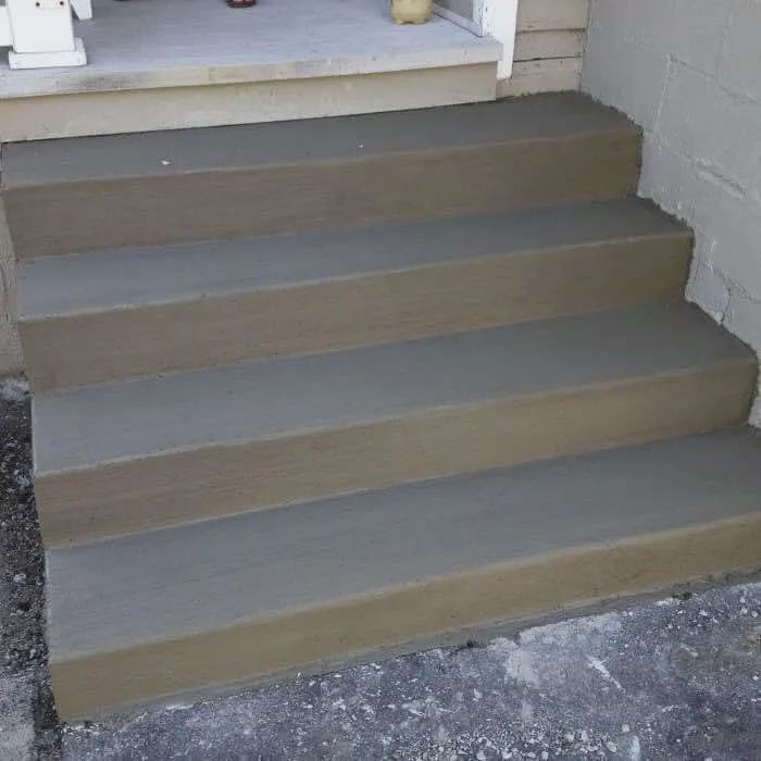 Four newly poured grey concrete steps leading up to a porch landing next to a cinder block wall.