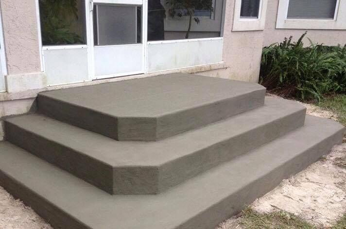 Three concrete steps leading up to a sliding glass door on a residential patio.