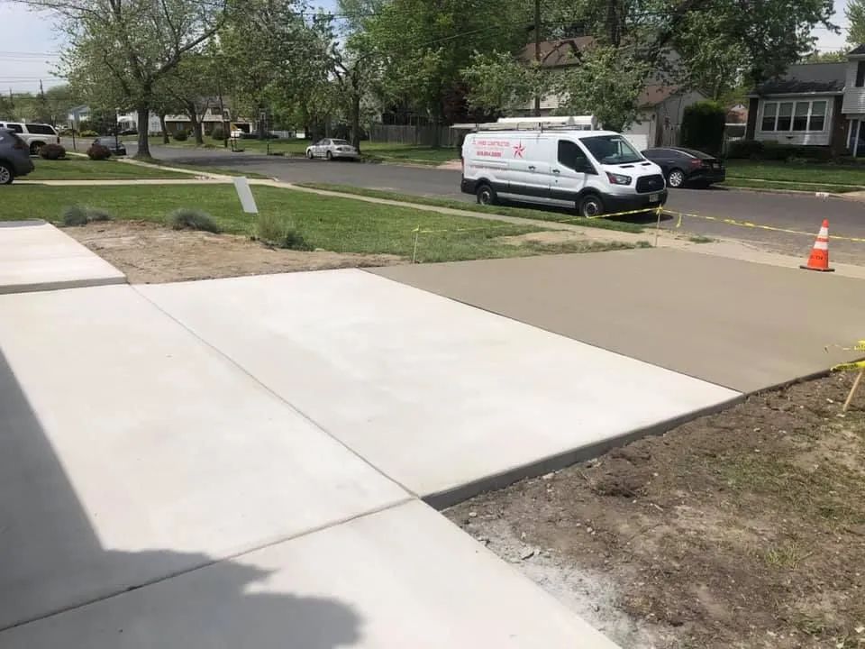A freshly poured concrete driveway in a suburban neighborhood with a white service van parked on the street nearby.