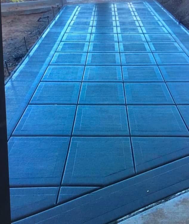 A freshly poured concrete driveway featuring a grid pattern of stamped square sections with darker border lines.