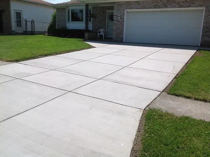 A freshly poured concrete driveway with a grid pattern leading to a brick garage and house entrance.