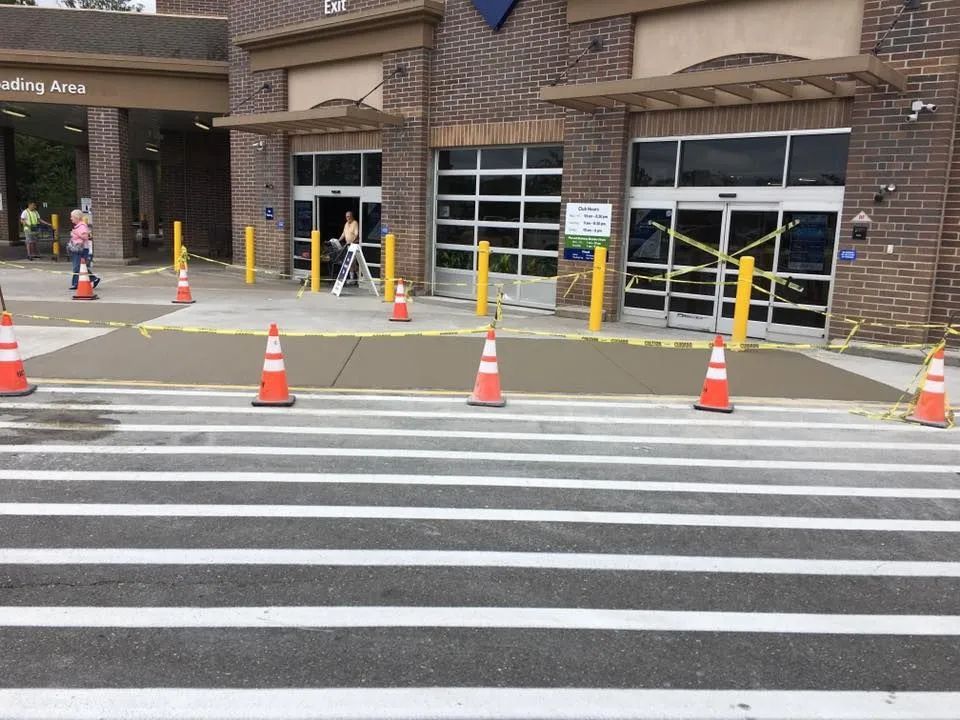 Orange traffic cones line a fresh concrete sidewalk repair area in front of a brick building entrance.