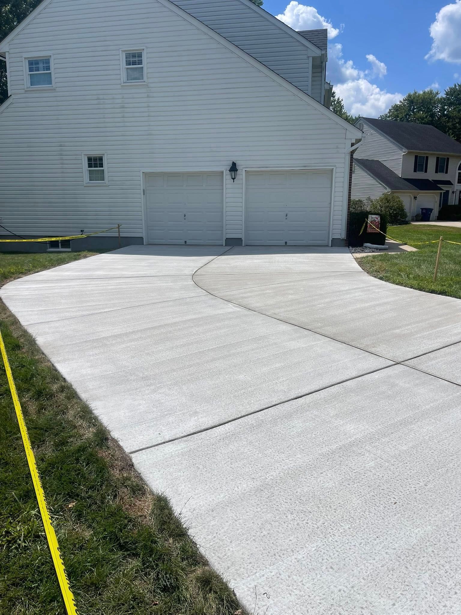 A white house with a two-car garage features a newly paved, light gray concrete driveway extending toward the foreground.