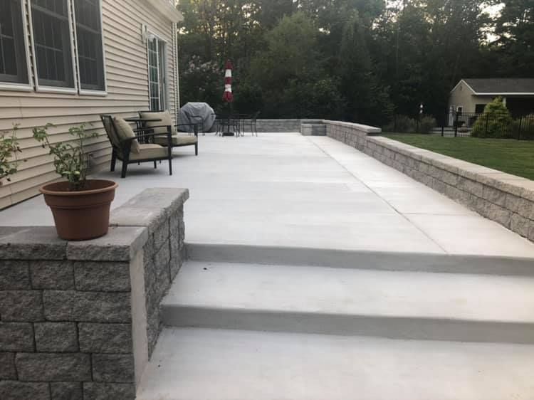 A concrete patio with stone retaining walls, steps, and a potted plant adjacent to a beige house exterior.