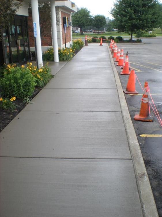 A sidewalk next to a building, lined with orange safety cones separating the walkway from a parking lot.