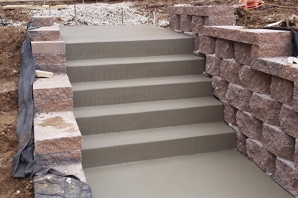 Freshly poured concrete stairs flanked by stone retaining walls at a construction site.