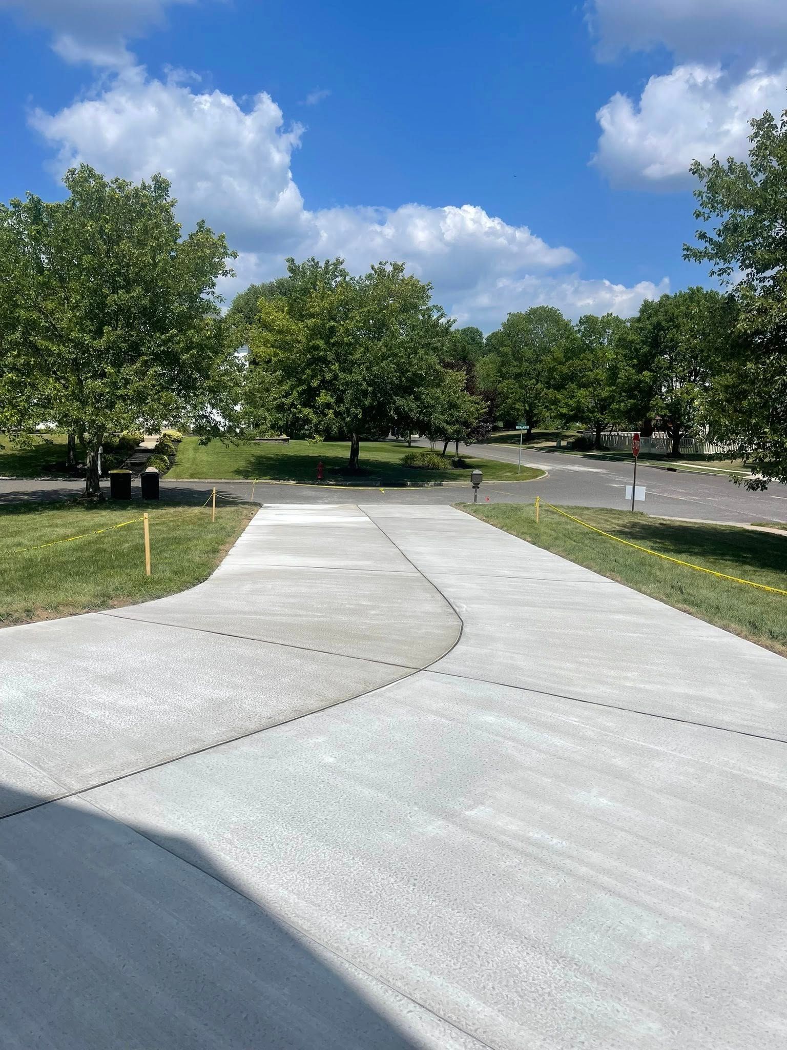 A concrete driveway splits into two paths in a sunny outdoor setting with grass and trees in the background.