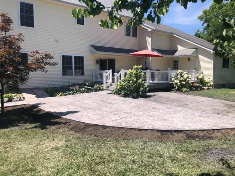 A light-colored two-story house with a stamped concrete patio, a wooden deck, and a red patio umbrella in the backyard.