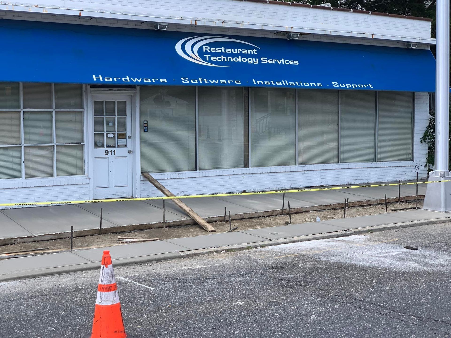 Storefront for Restaurant Technology Services with a blue awning, white door, and construction zone in front.