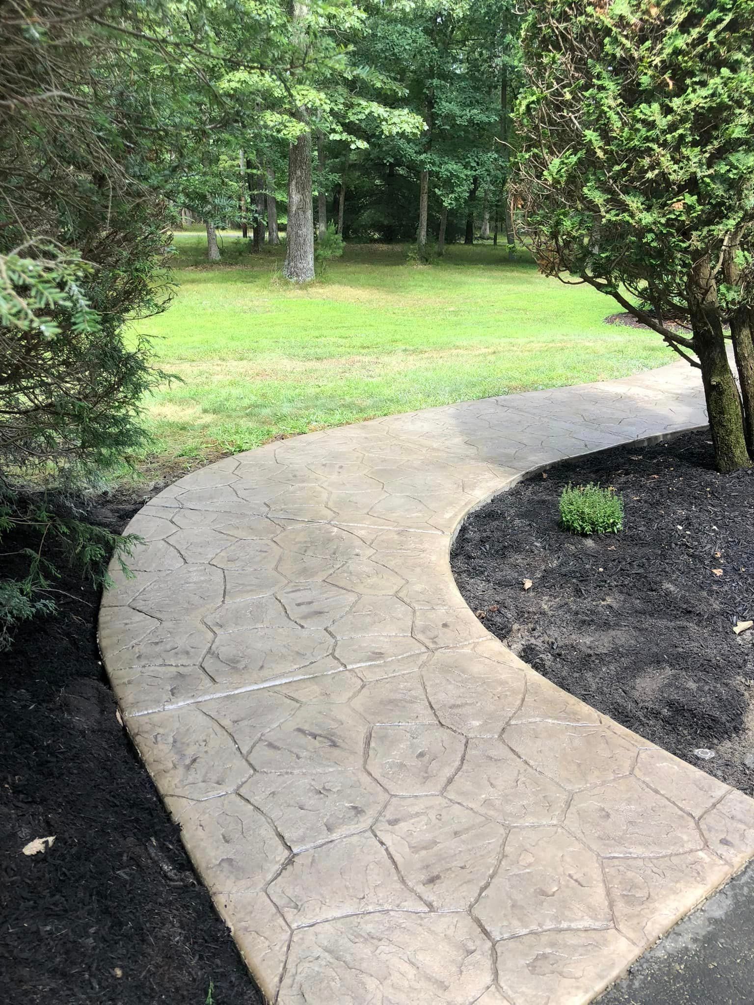 A curved stamped concrete walkway leads through a landscaped yard with green grass and trees.