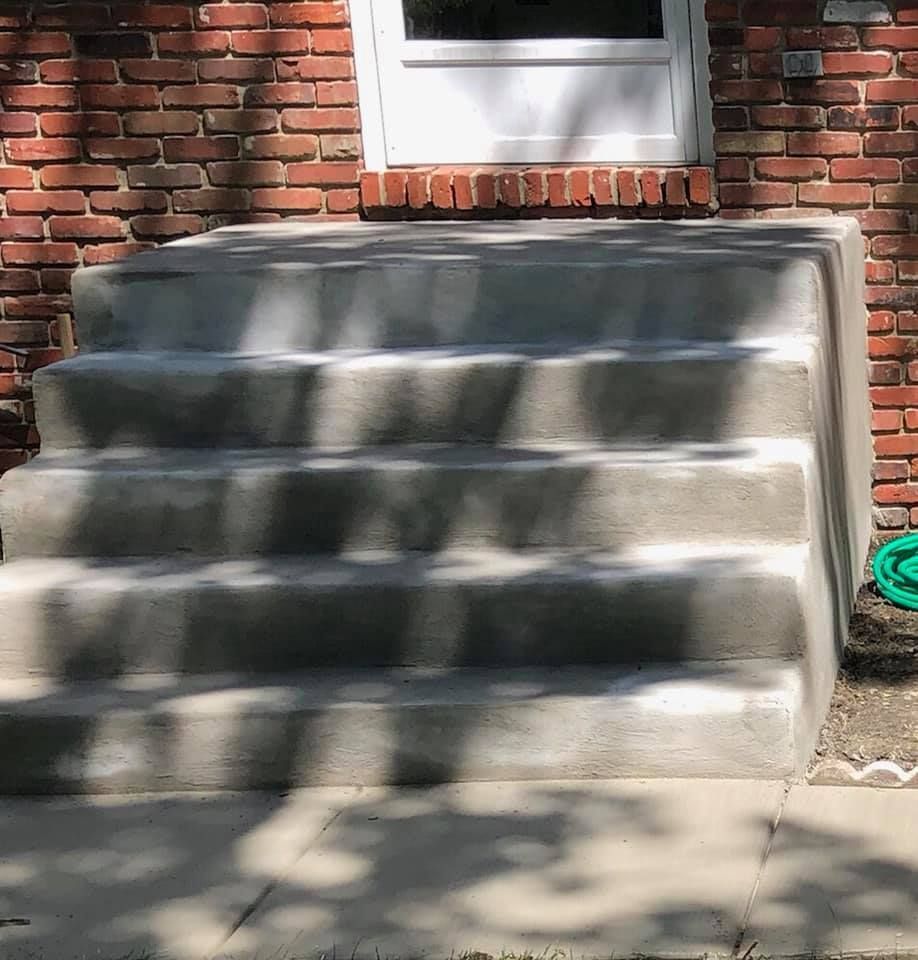 A set of four new gray concrete steps leading up to a white door on a brick house.