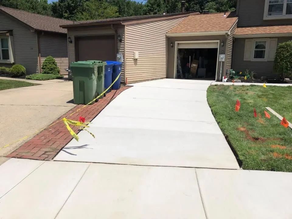 A newly poured concrete driveway leads to a suburban home garage with a brick border on the left and grass on the right.