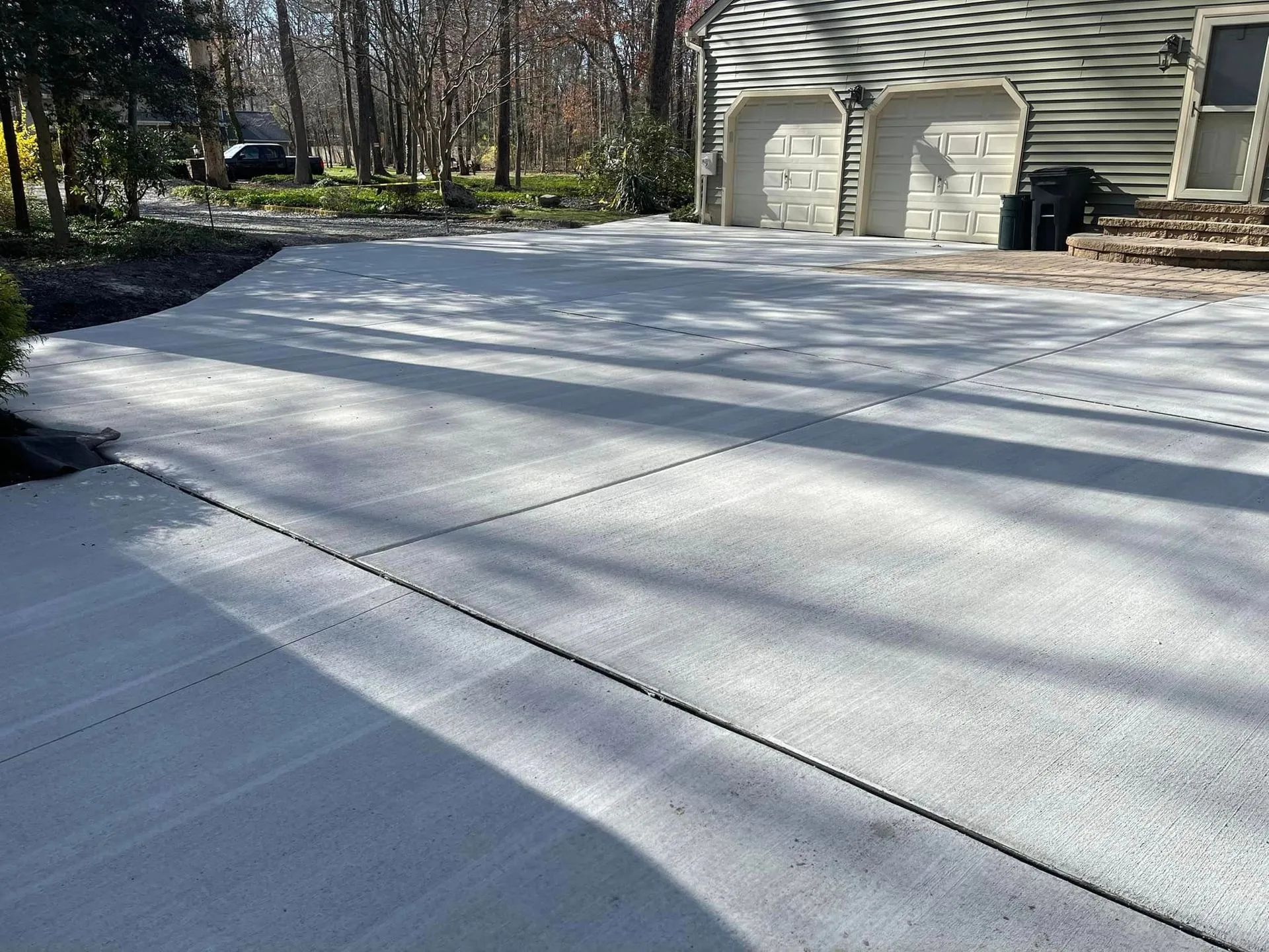 A newly poured concrete driveway leads to a two-car garage of a house, with trees visible in the background.