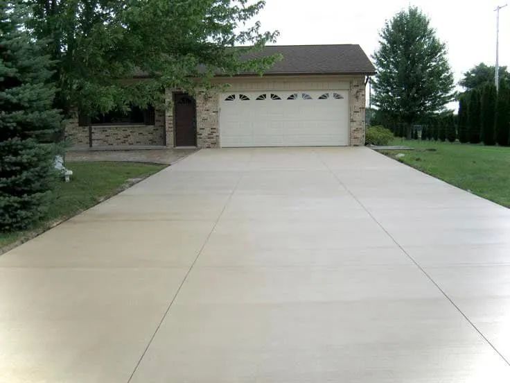 A clean, light-colored concrete driveway leads to a two-car garage of a suburban house.
