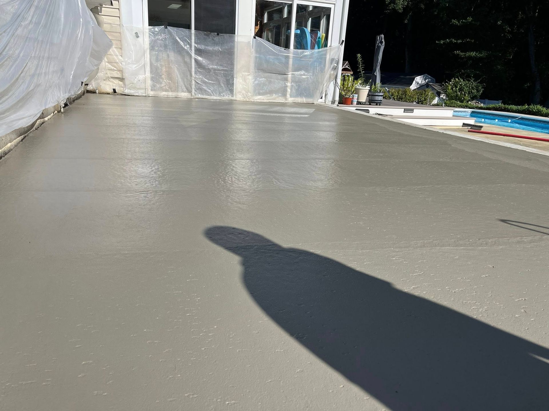Freshly poured concrete patio next to a swimming pool, partially covered by protective plastic sheeting.