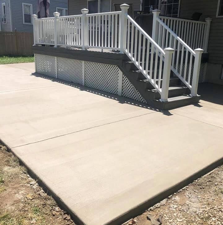A gray concrete patio sits in front of a raised wooden deck with white railings and white lattice skirting.