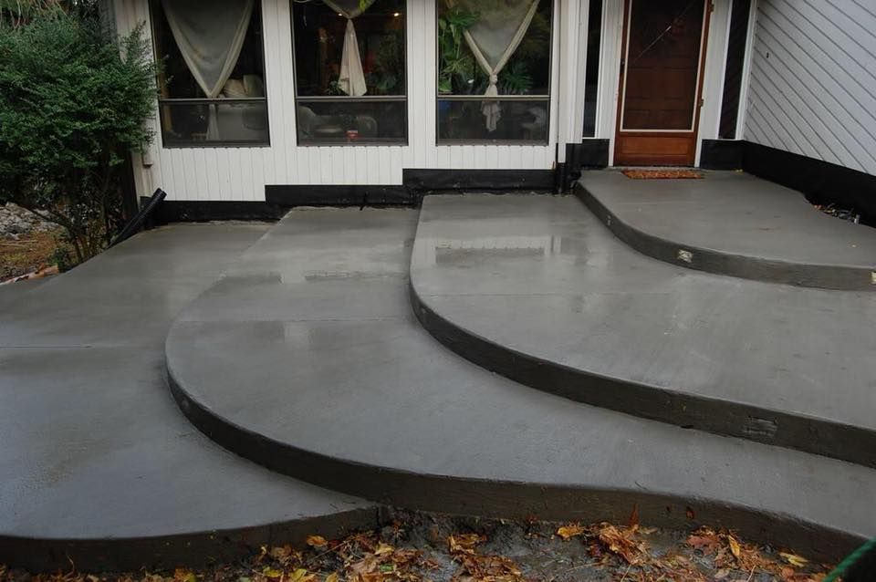A house exterior featuring a freshly poured, multi-level concrete patio with curved steps leading up to the front door.