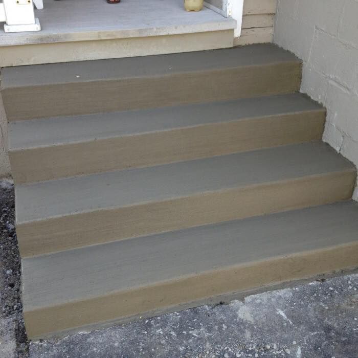 A set of four freshly poured gray concrete steps leading up to a house entrance.