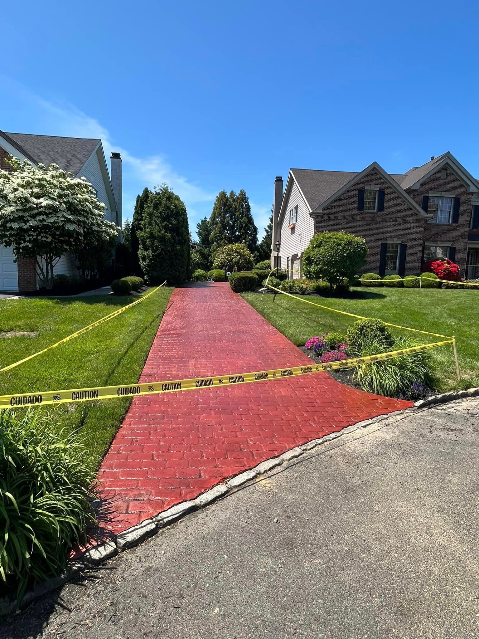 A bright red brick driveway leads between two houses, blocked off by yellow caution tape stretched across the entrance.