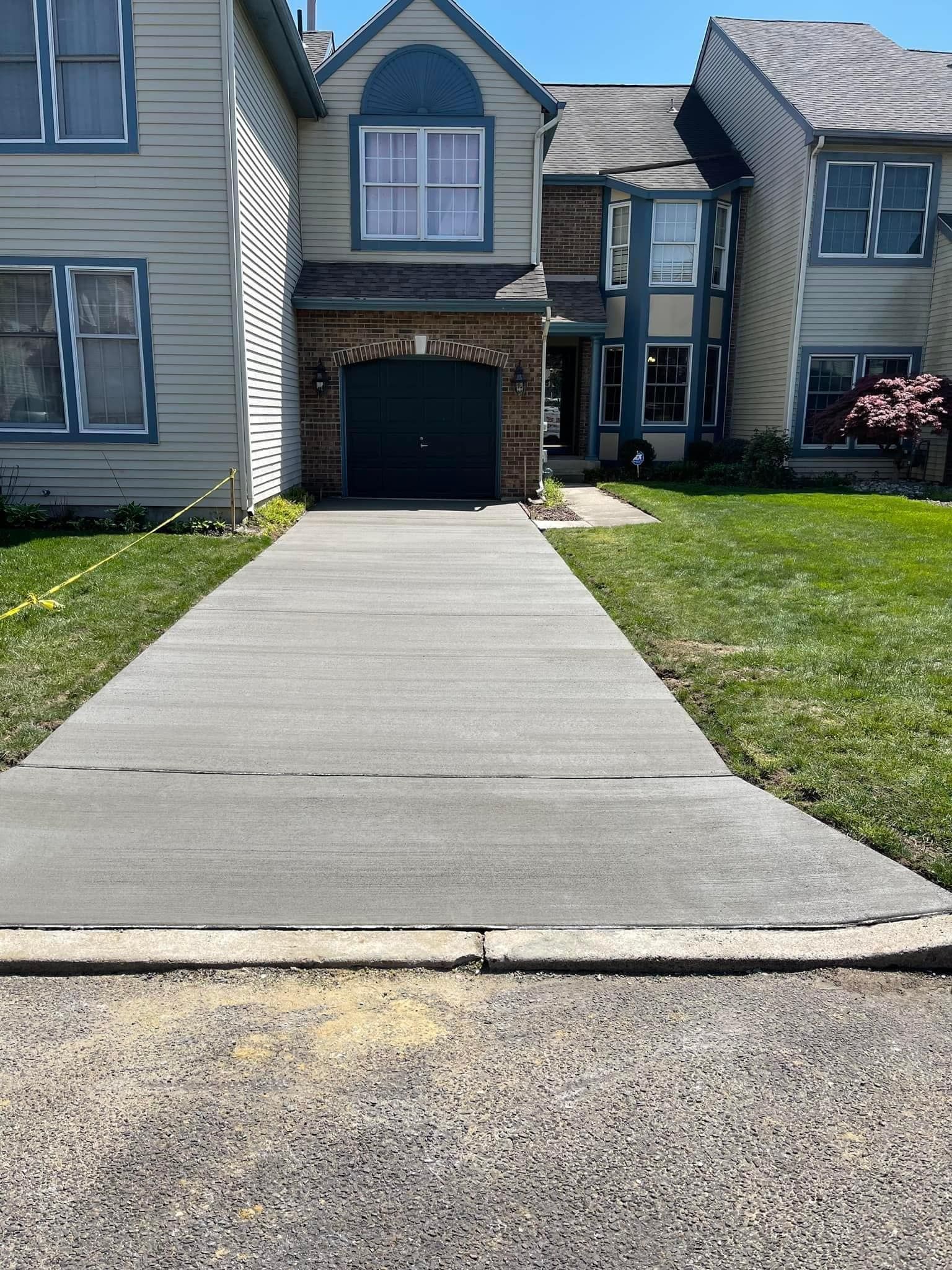 A newly poured concrete driveway leads to the garage of a beige multi-level home on a sunny day.