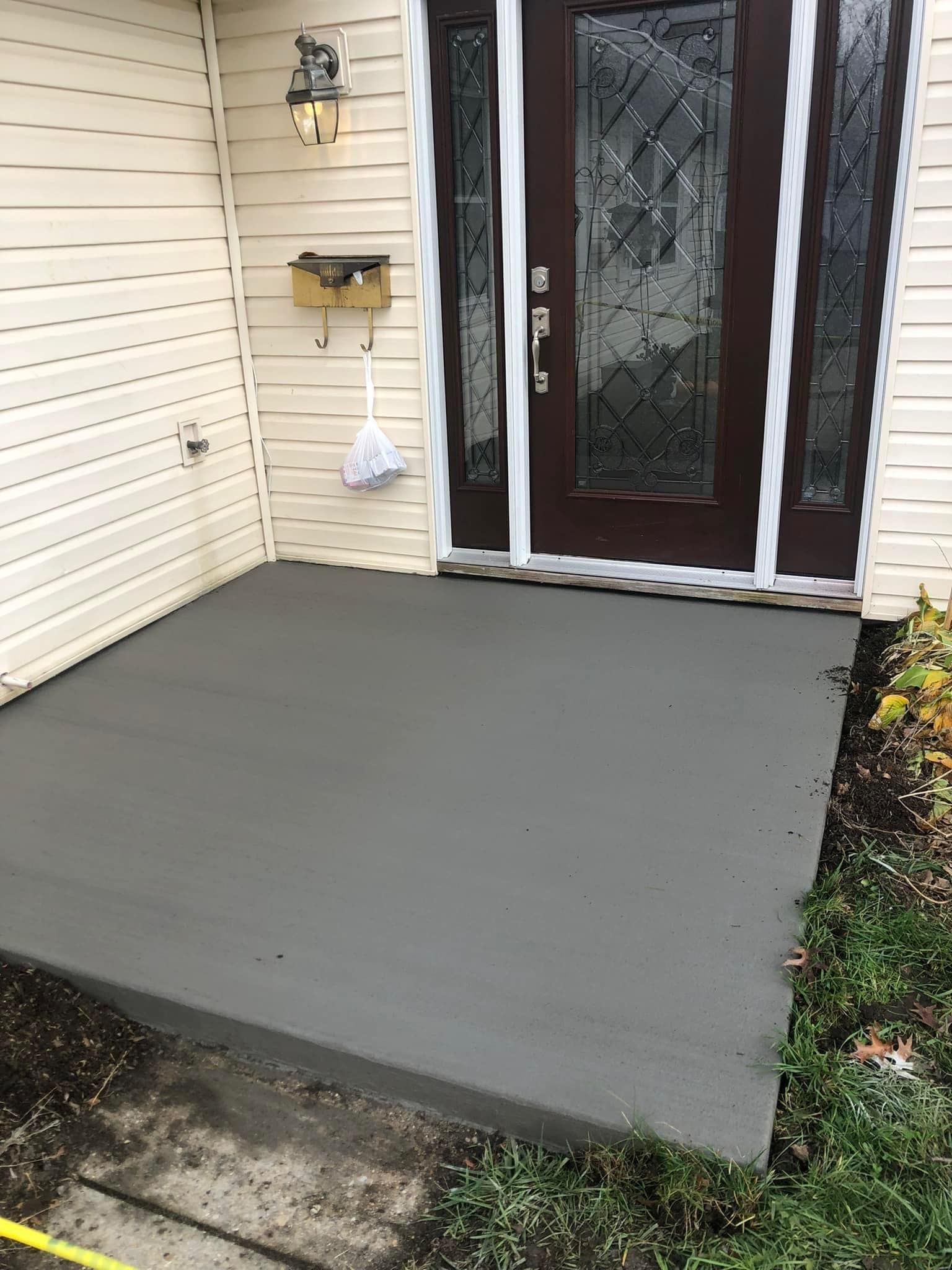 A freshly poured, smooth gray concrete porch in front of a house entrance with a brown door and light siding.