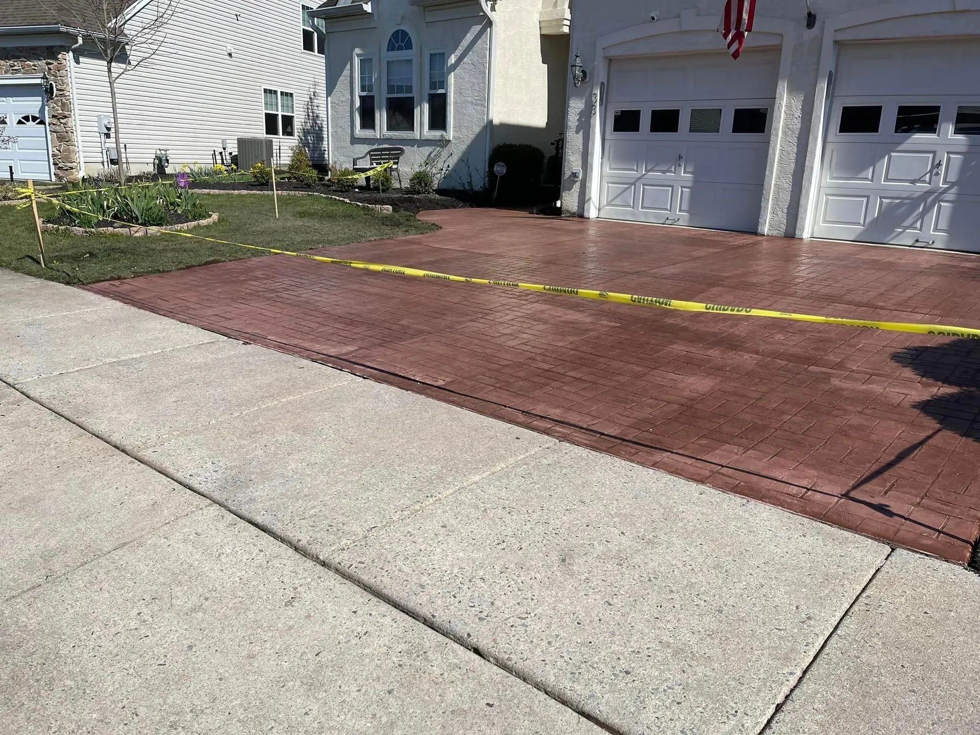 A residential driveway with stamped, reddish-brown concrete, blocked off by yellow caution tape.