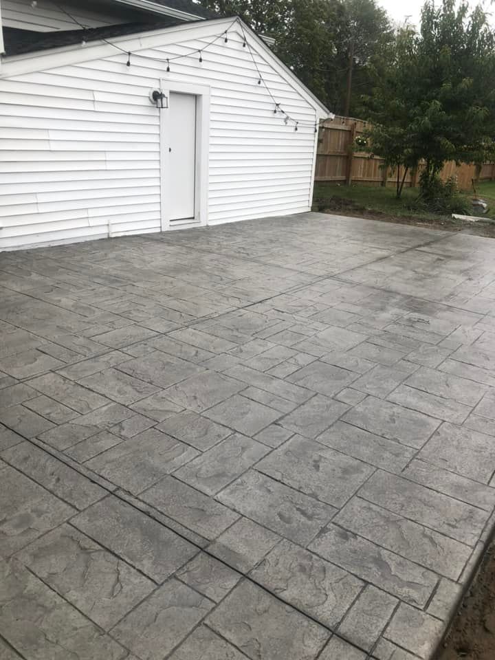 Gray stamped concrete patio with a rectangular pattern leading to a white building exterior with string lights.