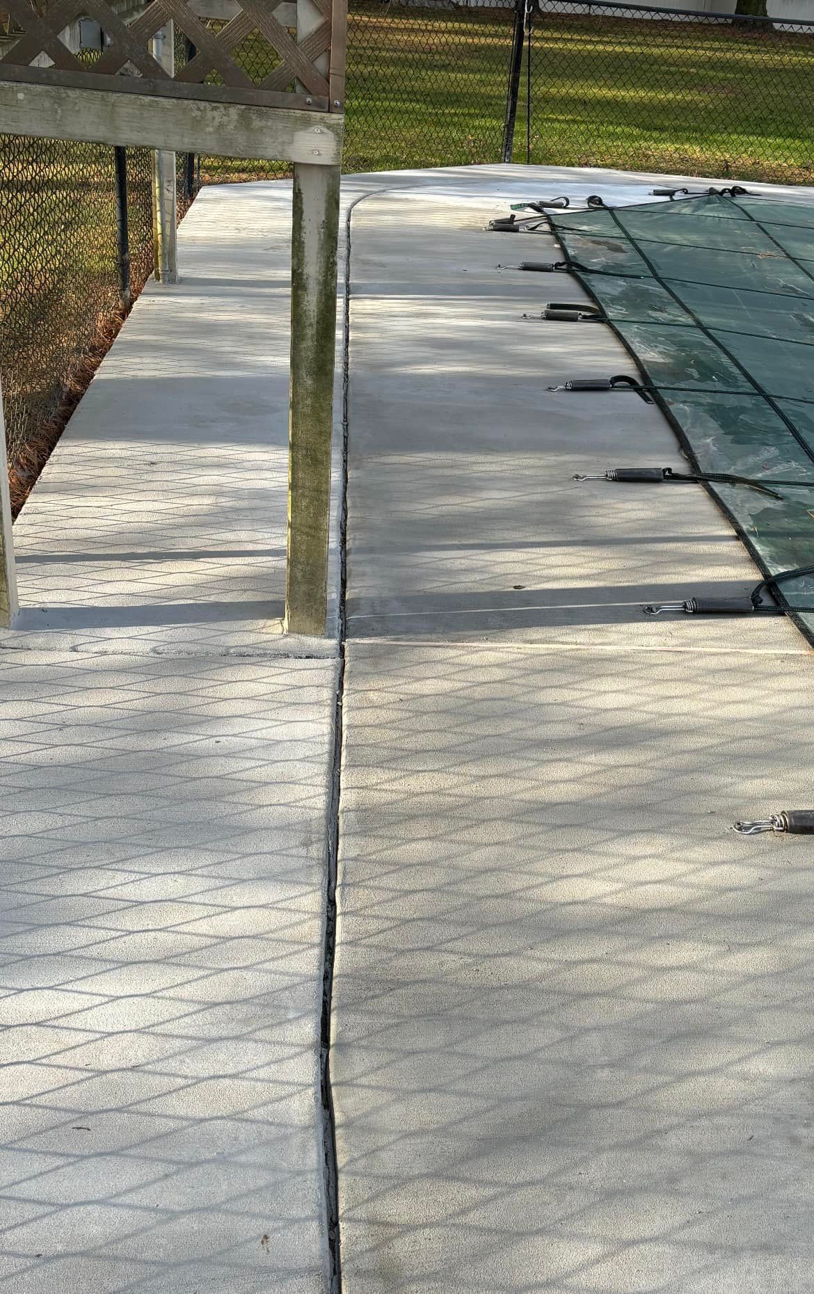 A paved walkway with a noticeable gap between the concrete sections runs alongside a swimming pool covered by a tarp.