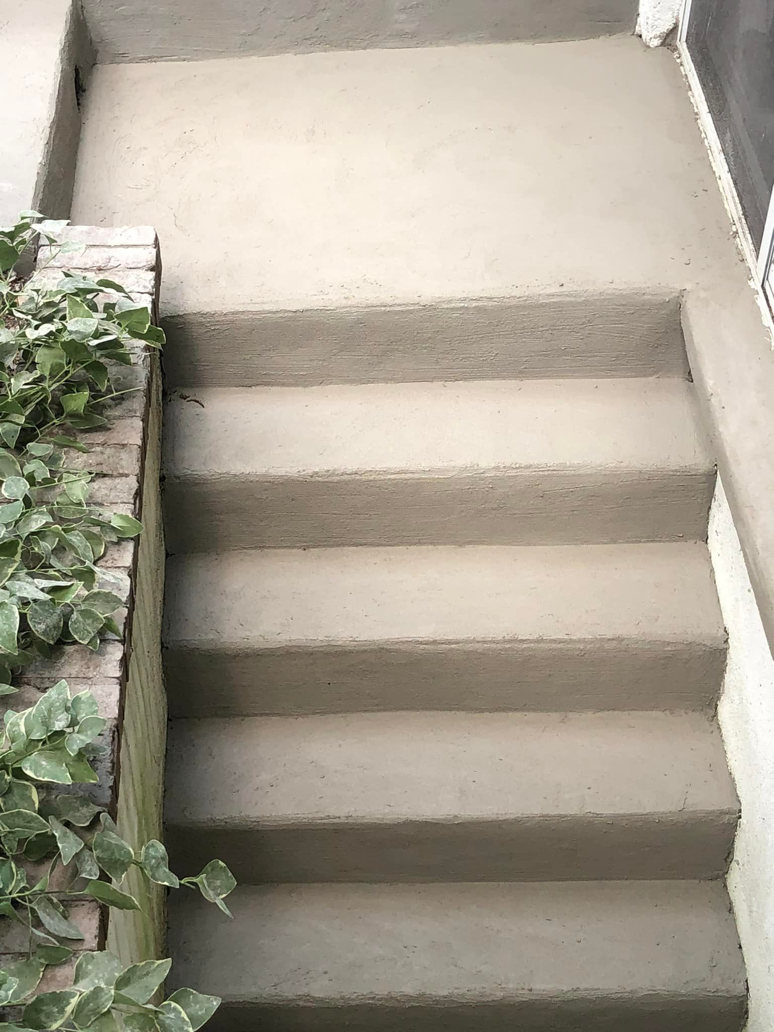 A set of four freshly finished concrete outdoor steps leading up to a small landing, bordered by a brick planter.