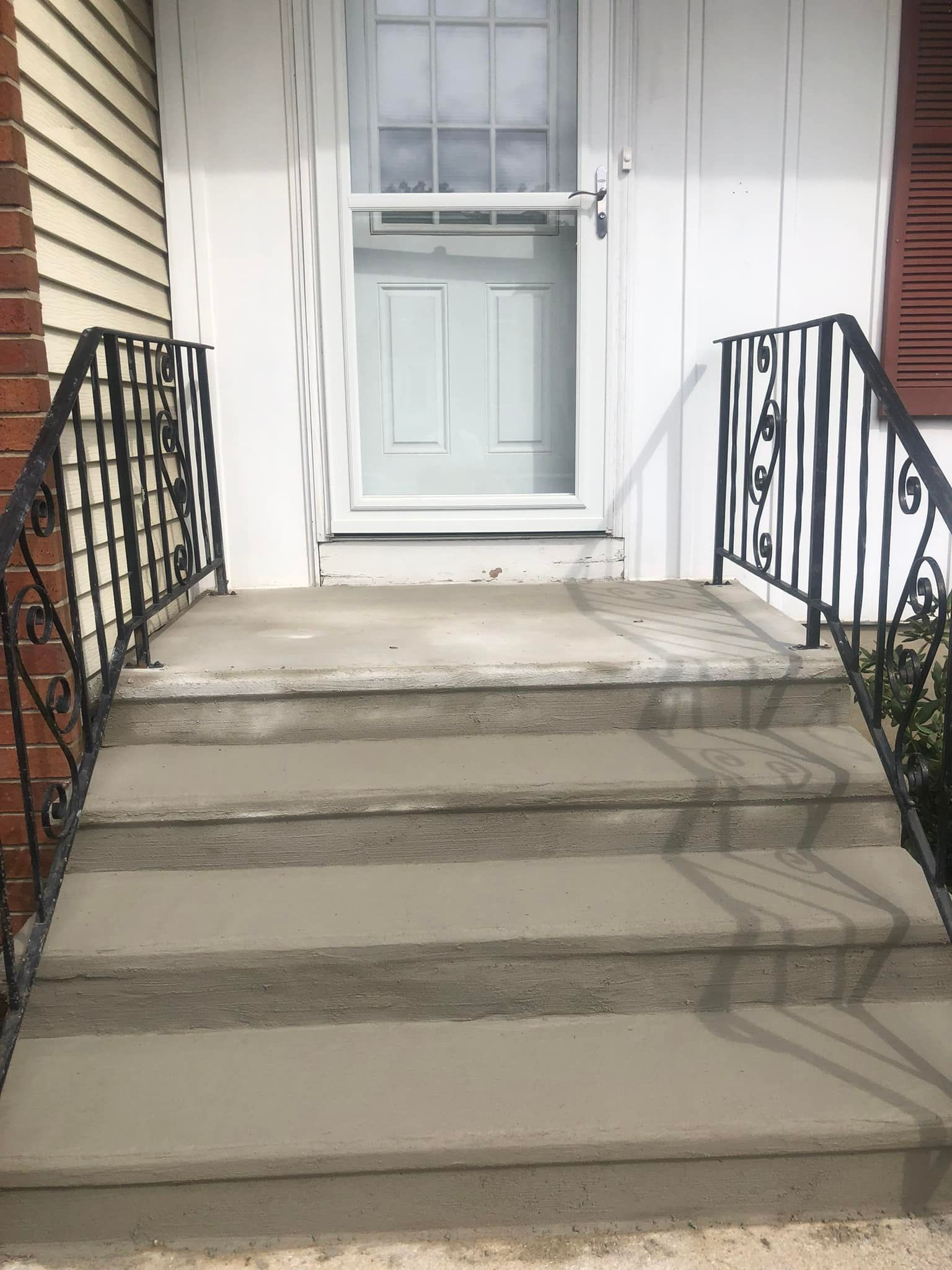 Concrete front steps leading to a house door, flanked by black decorative metal railings.