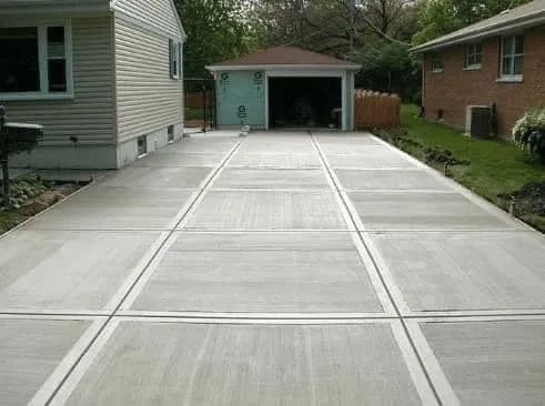 A newly poured, light gray concrete driveway with clean, grid-patterned control joints leading to a detached garage.