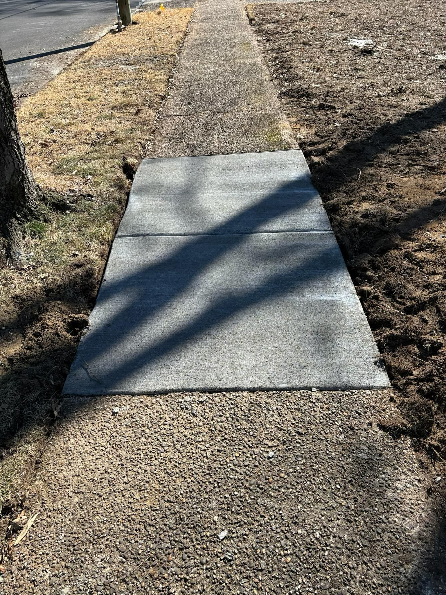 A sidewalk with a newly installed smooth concrete patch contrasting against the original weathered, textured pavement.