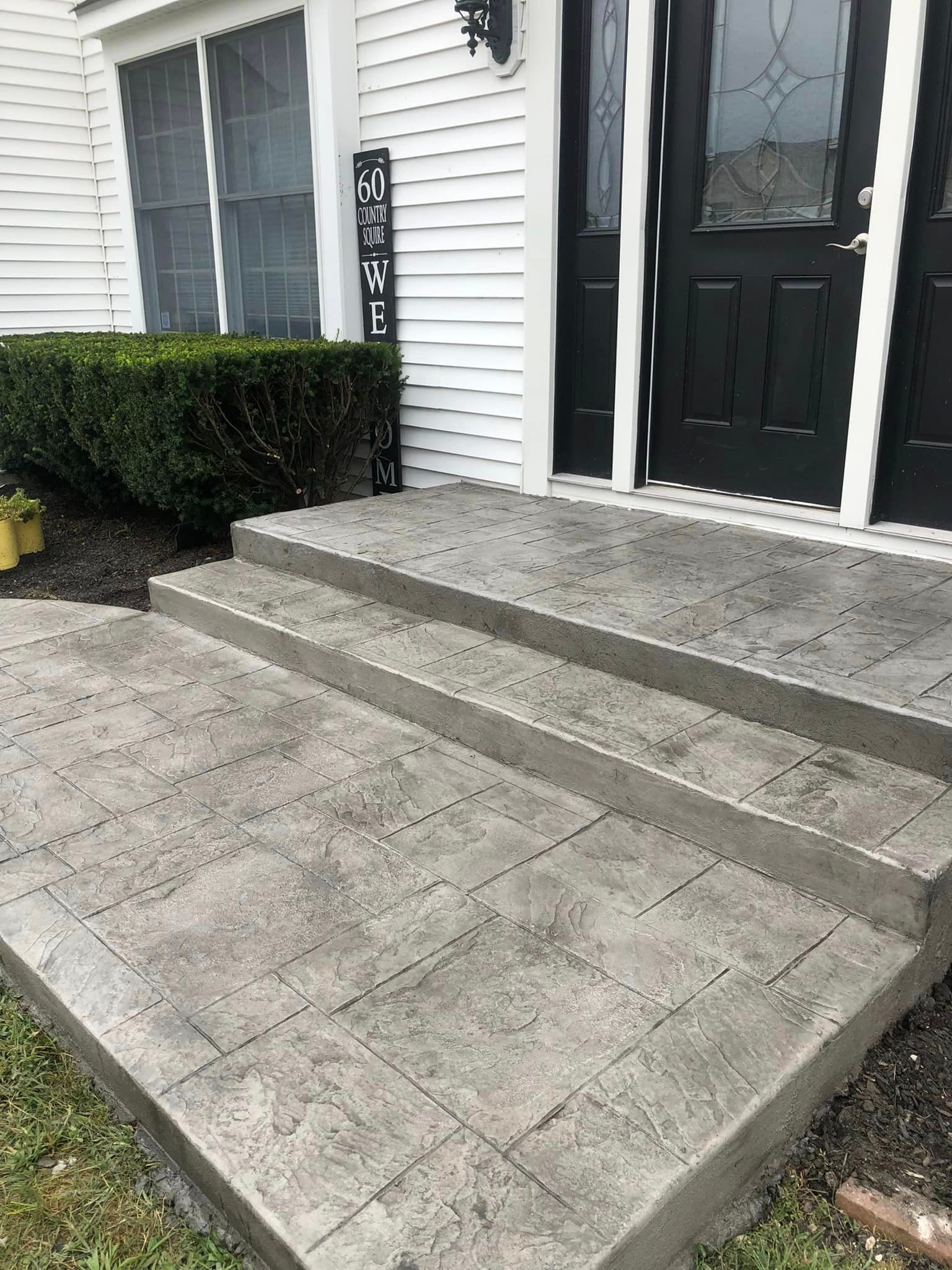 Stamped concrete front steps and a small landing leading to a black double door with glass inserts on a white house.