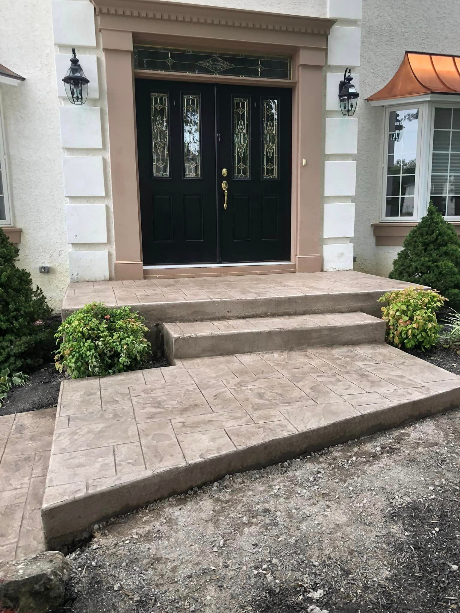A set of concrete stairs and a walkway leading to a black double front door with decorative glass panels.