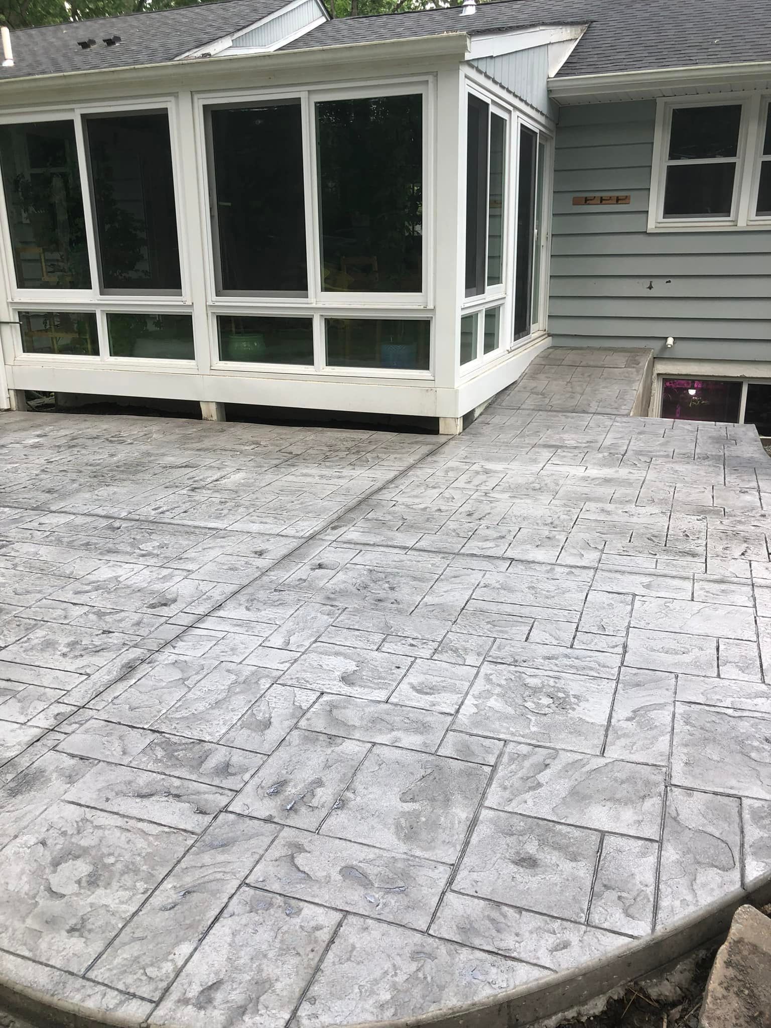 A gray patterned concrete patio extending from a light blue house with a white-framed sunroom.