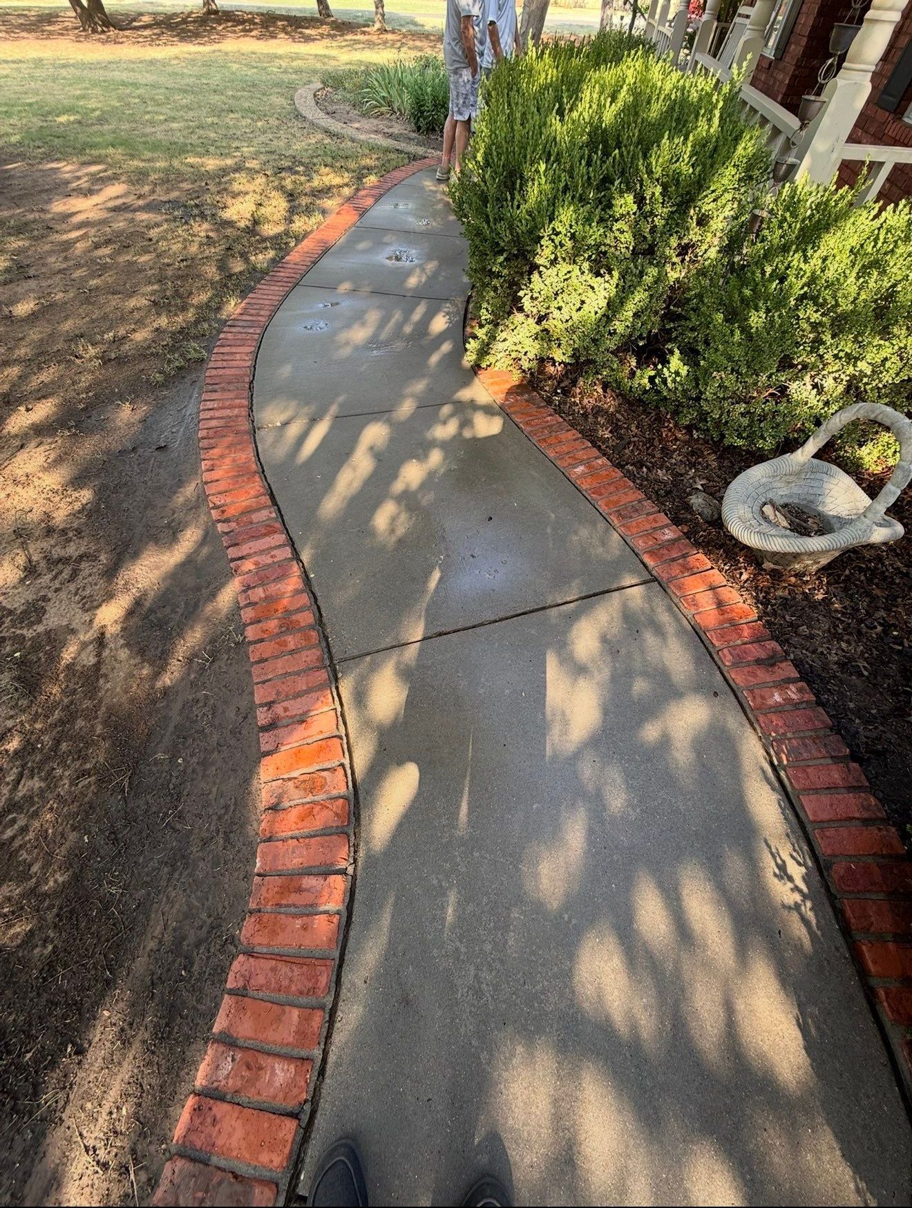 Curved concrete walkway bordered with red bricks beside shrubs and a lawn