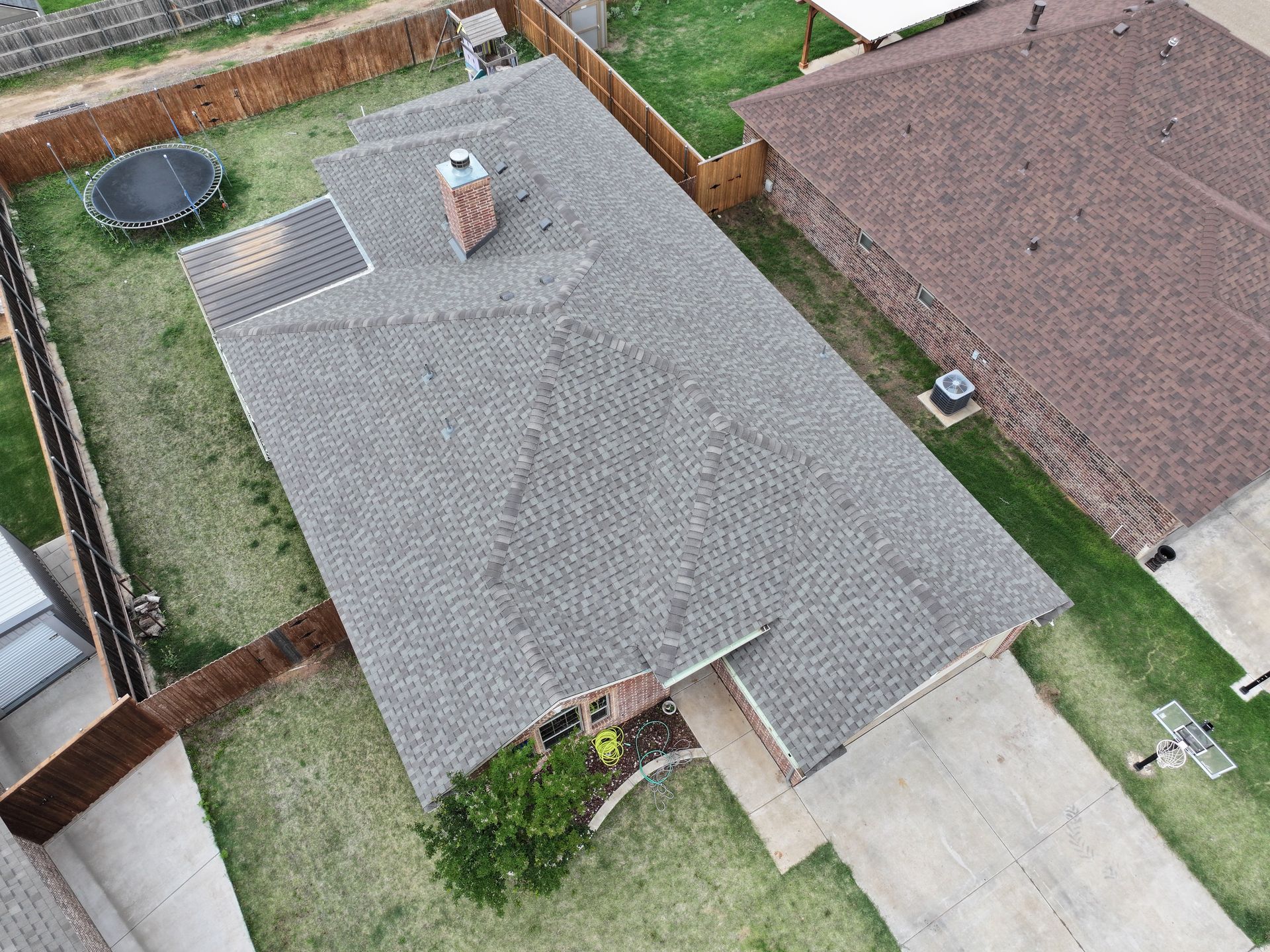Aerial view of a house roof with a chimney, driveway, and fenced yard.
