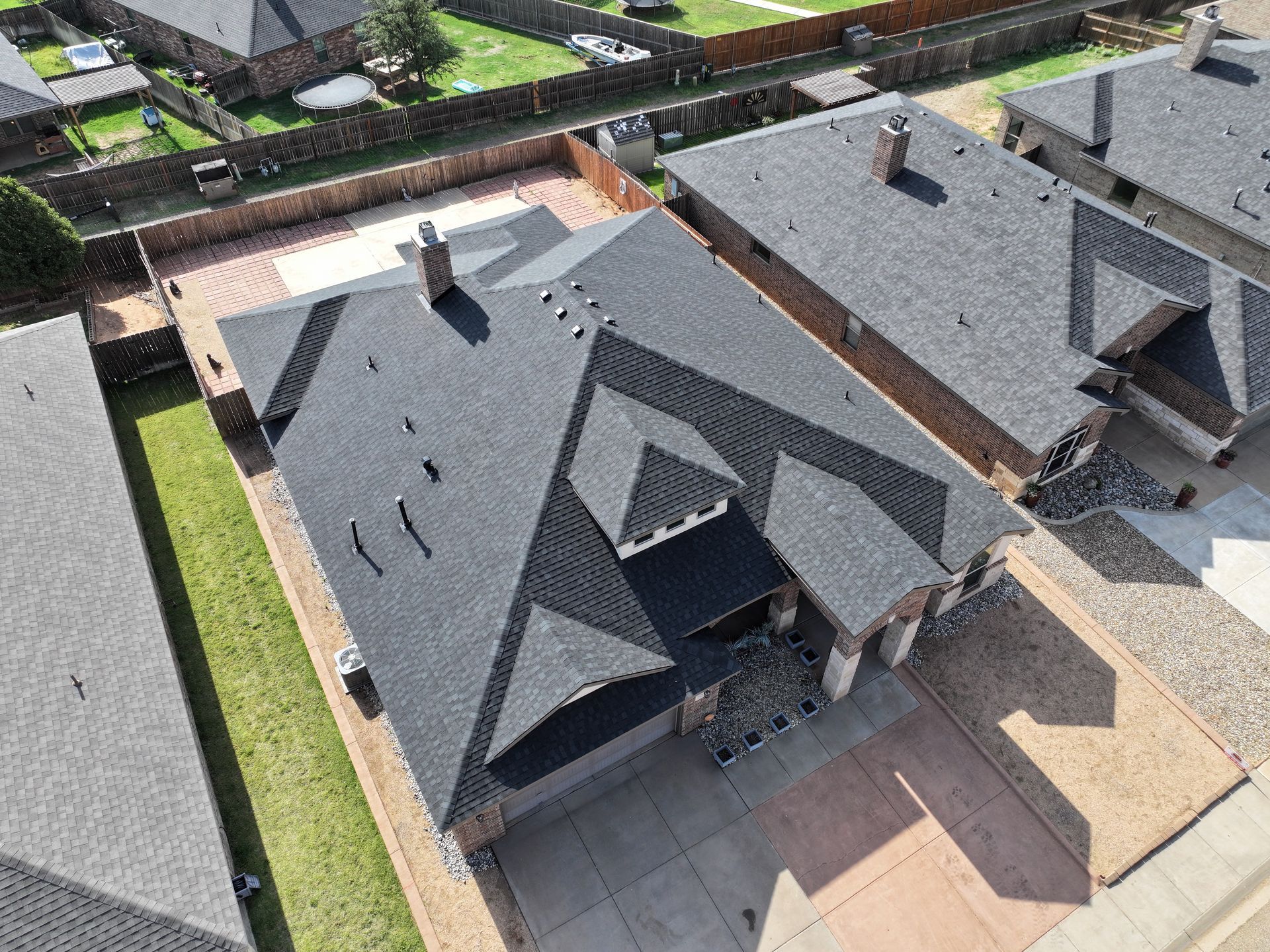 Aerial view of a modern house with a dark shingled roof and gray siding in a suburban neighborhood