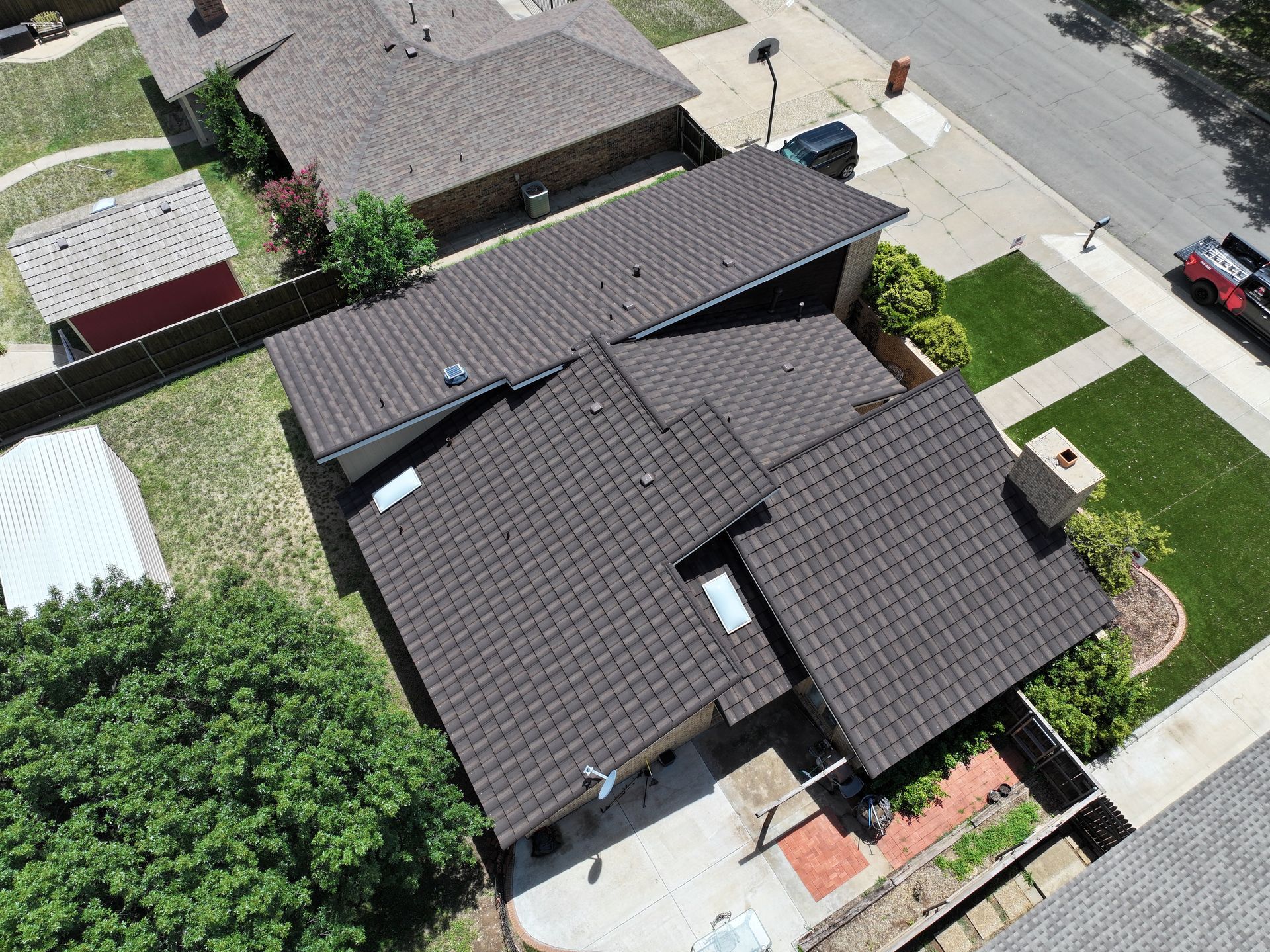Aerial view of a dark-roofed suburban house with a driveway, lawn, and neighboring homes.