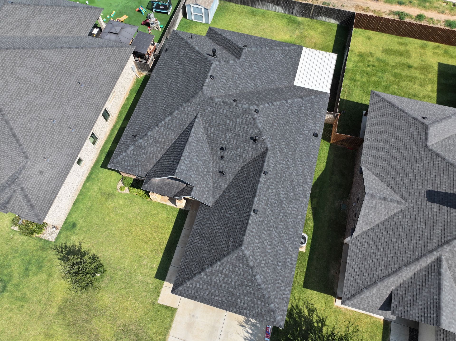 Aerial view of dark gray-roofed suburban houses with green lawns and driveways.