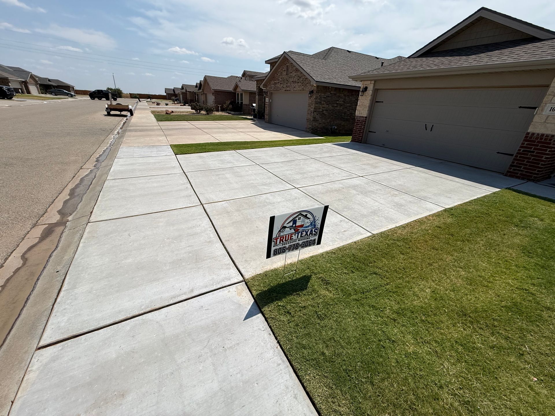 Suburban driveway and lawn with a small real estate sign near the sidewalk