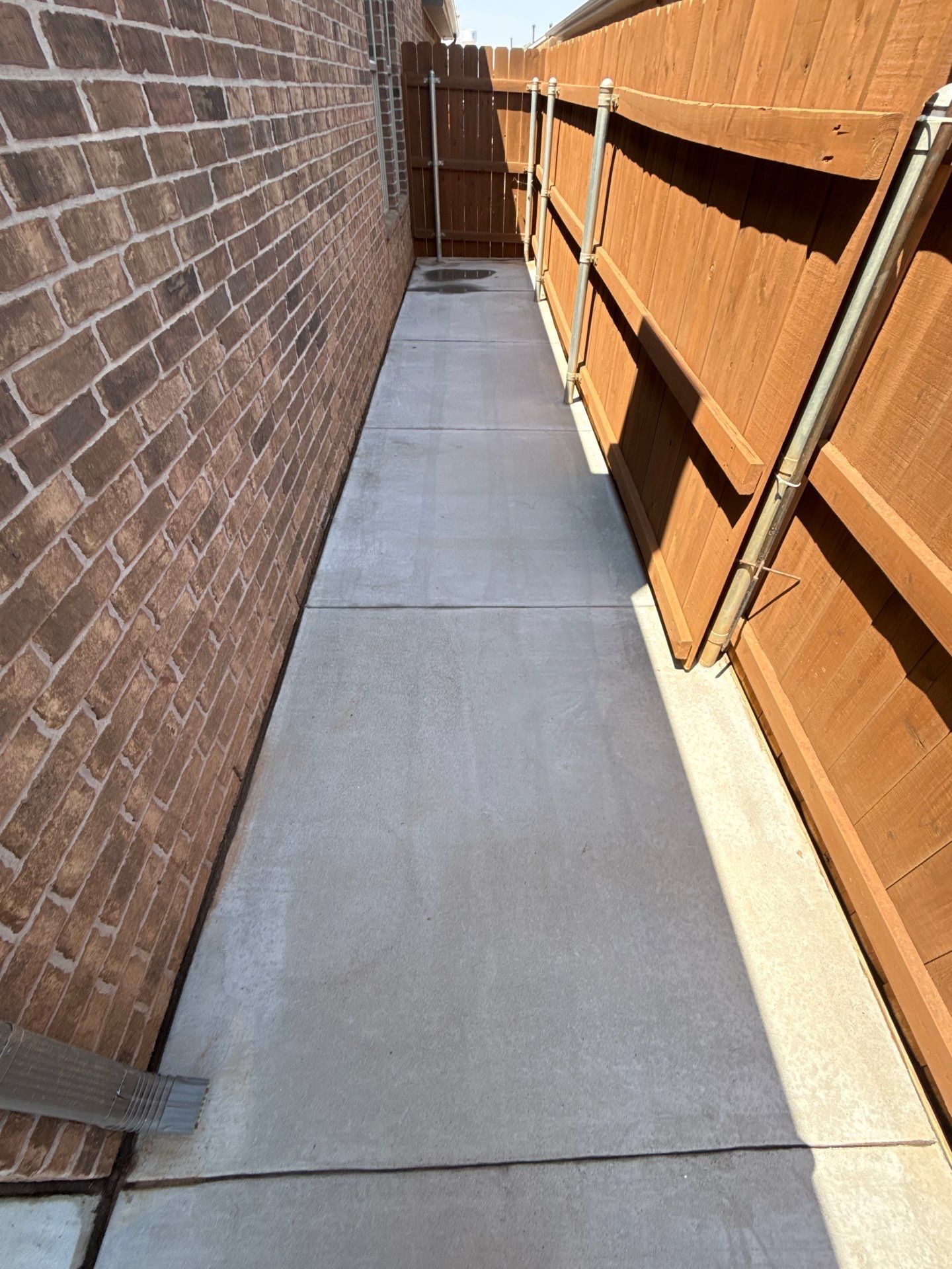 Narrow concrete walkway between a brick wall and wooden fence, ending at a gate.