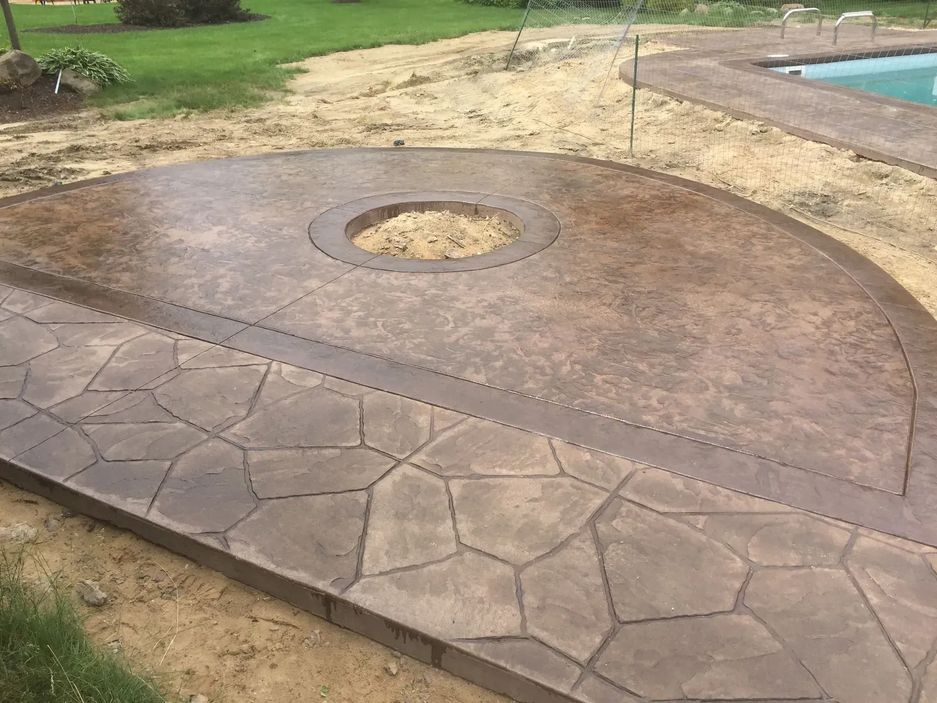 A concrete patio with a fire pit in the middle next to a pool.