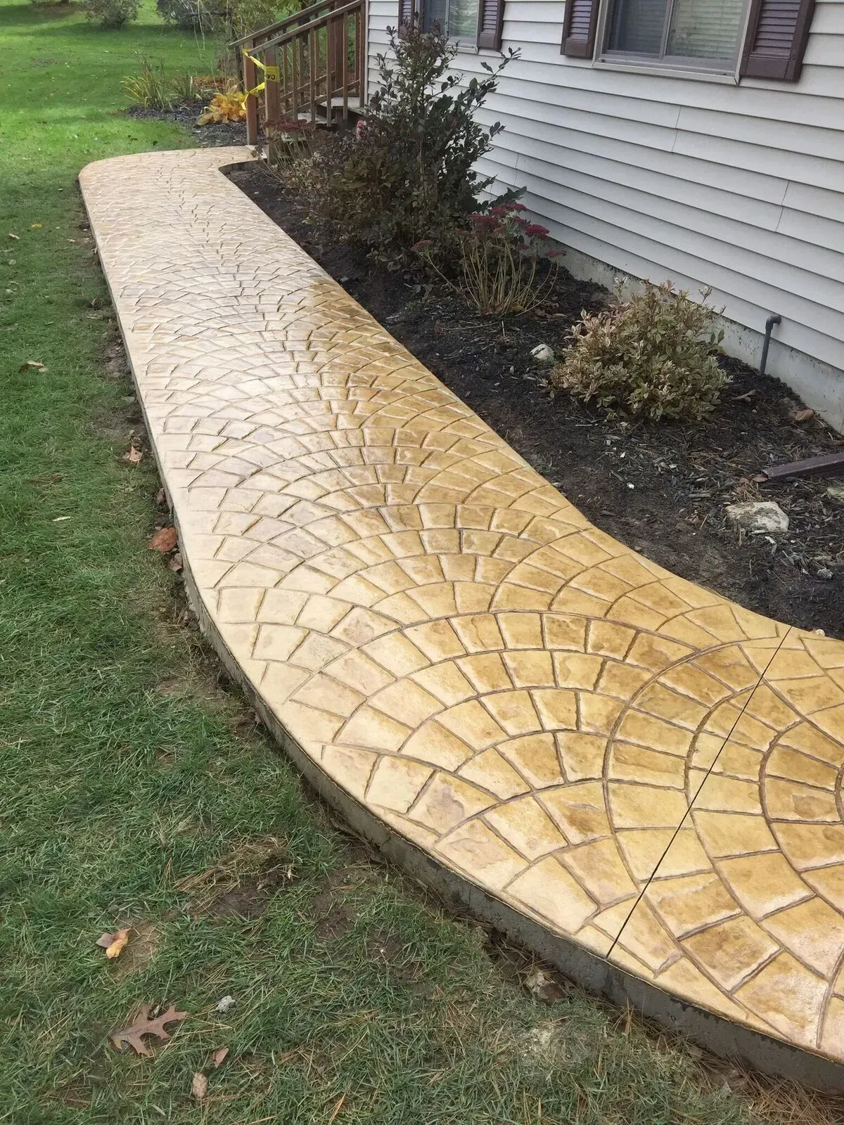 A concrete walkway leading to a house next to a lawn.