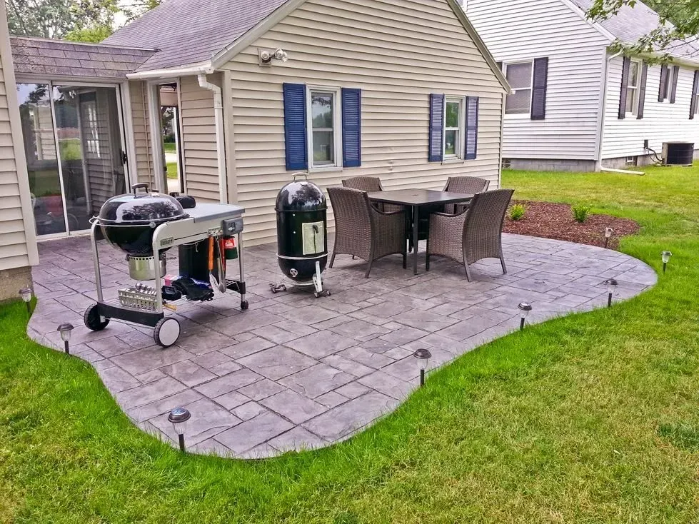 A patio with a table and chairs and a grill in front of a house.
